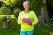 Portrait of smiling biracial senior woman wearing sports clothing holding yoga mat against plants