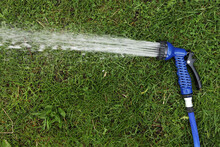 Blue Gun Spray Water On The Hose For Watering The Lawn. Blue Spray Gun For Watering Green Grass. Irrigation Of The Garden With A Garden Hose. Gardening. Farming. Agriculture. Place For Your Text