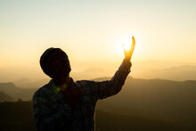 Silhouette Rosary Against Cross In Hand. Background Sunrise