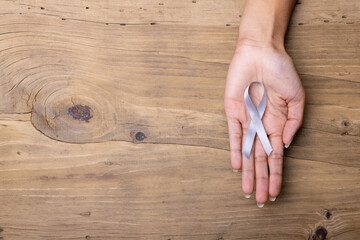 Hand of african american mid adult woman with white lung cancer awareness ribbon wooden table