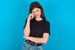 © Jihan - Unhappy young caucasian woman wearing black T-shirt over blue background crying while posing at camera whipping tears with hand.