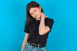 © Jihan - young caucasian woman wearing black T-shirt over blue background suffering from back and neck ache injury, touching neck with hand, muscular pain.