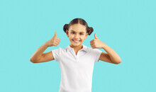 Happy Kid. Joyful Child In Cotton Tennis Tee Says Well Done, Yes, Okay, Excellent, Perfect. Girl In Polo Tshirt, With Cute Hair Buns Standing Isolated On Blue Looks At Camera, Smiles, Gives Thumbs Up