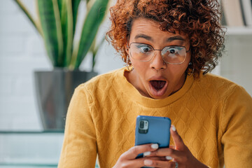 woman or girl at home looking at mobile phone or smartphone surprised