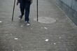 Alte Frau mit blauen Hosenbeinen und Sandalen mit zwei Stöcken auf Straße 