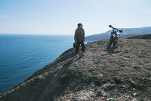 Girl Motorcyclist Standing On The Edge Of  Cliff Holding Helmet In Her Hand, Resting After Difficult Off-road Climb On  Dirt Bike