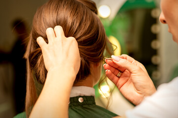 Hairstyling bride. A female hairdresser makes styling hair for the beautiful young caucasian woman in a beauty salon