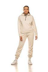 Wall Mural - Front view of a young woman in a beige tracksuit posing to a white background in the studio