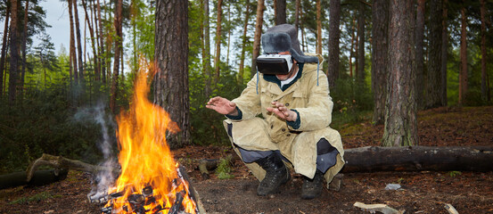 Wall Mural - Hiking in the forest and virtual reality. A man wearing virtual reality glasses in the forest near a campfire.