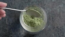 Pouring Green Barley Grass Powder Into A Glass Of Water - Preparation Of A Healthy Drink