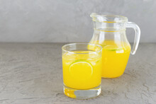 Homemade orange lemonade in a glass and jug on a gray background.