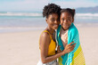 © WavebreakMediaMicro - Portrait of smiling african american young mother wrapping daughter with towel against sea and sky