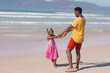 © WavebreakMediaMicro - African american girl holding young father's hands while enjoying at beach against sea on sunny day