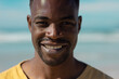 Close-up portrait of handsome smiling african american young man at beach against sky on sunny day