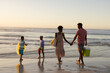 © WavebreakMediaMicro - Rear view of african american young couple holding hands while children playing at beach against sky