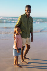 Portrait of happy african american young man standing with son against sea and clear sky at sunset