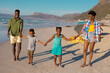 © WavebreakMediaMicro - Happy african american young parents and children holding hands while standing at beach against sky