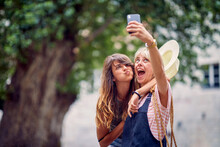 Young Women Making Funny And Goofy Face Expressions And Taking Selfie, On Street. Young Women Walking On Street Of European City. Travel, Fun, Togetherness Concept.