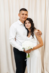 Smiling wedding couple posing in front of a white curtain.