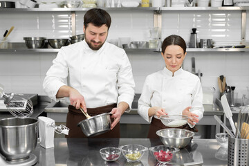 Pastry chef a man and a woman in a professional kitchen prepare a sponge cake, mix the ingredients and sift the flour.