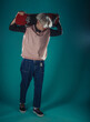 © qunica.com - Young adult man in casual outfit wear looking at camera, holding skateboard near face and standing at studio on blue background