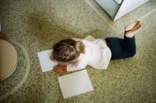 Little Girl Lays On Floor And Writes And Draws