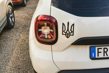 The State Emblem of Ukraine on a white body of a car with an EU license plate on an asphalt road, European solidarity with the people of Ukraine in the fight against Russian aggression