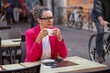 © Anna Berkut/Stocksy - portrait of business woman in pink jacket drinks coffee in street cafe