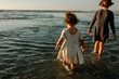 © Erin Brant/Stocksy - Back of sisters in dresses wading in ocean