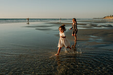 Girls In Dresses Running On Beach At Sunset