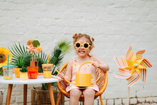 Girl With Bright Colored Watering Can And Flower Sunglasses Outdoors