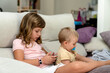 © Albert Martinez/Stocksy - Girl using smartphone while sitting with baby on couch