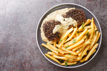 Classic French dish steak au poivre is a filet mignon with a crunchy peppercorn crust and rich Cognac sauce served with french fries close-up in a plate on the table. Horizontal top view from above