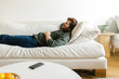 © STUDIO TAURUS/Stocksy - Smiling caucasian male lying on living room sofa