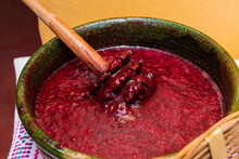 Closeup Of A Clay Pot With Red Prickly Pear Juice And A Wood Grinder