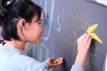 Closeup Little Asian Girl Creating Chalk Drawing On Blackboard
