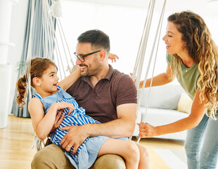 Wall Mural - child daughter family happy mother father sofa playing fun together girl cheerful smiling home indoor swing