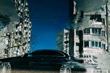 Reflection Of Apartment Buildings And A Car In A Puddle.