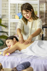 Wall Mural - Asian young oriental professional female masseuse therapist stand massaging shoulder and back of spa customer covered by white clean bath towel lay down resting relaxing closed eyes on massage bed