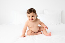 Joyful Chubby Baby Sitting On White Bed