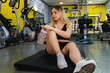 A young woman is stretching and drinking water in the gym after a workout during the day