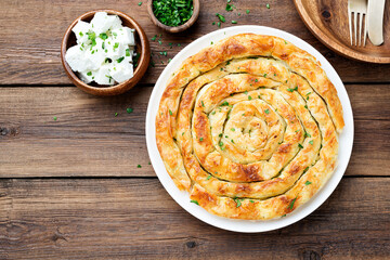 Wall Mural - Traditional feta cheese phyllo pastry pie on wooden background .