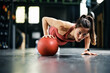 Female athlete doing single arm medicine ball push-up while working out in gym.