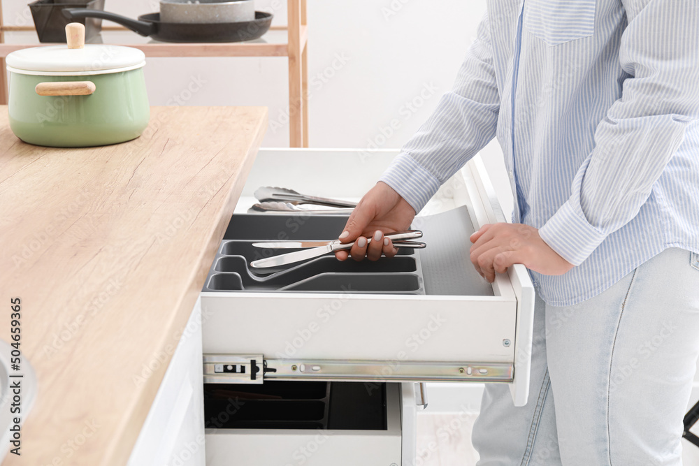 Woman taking silver knife from open drawer in kitchen