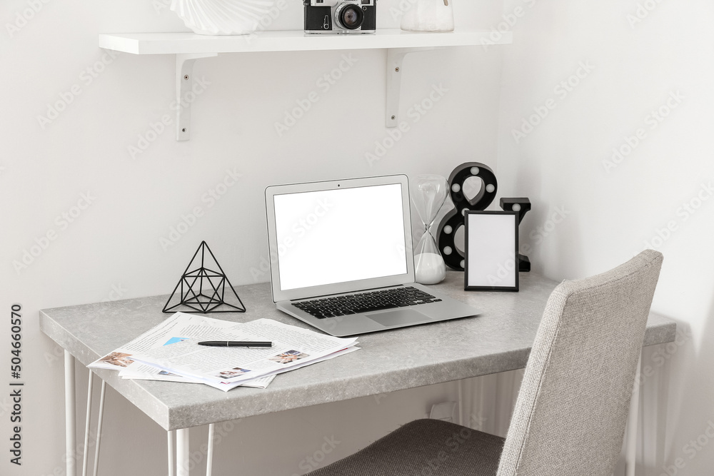 Workplace with modern laptop, newspapers and stylish decor near light wall