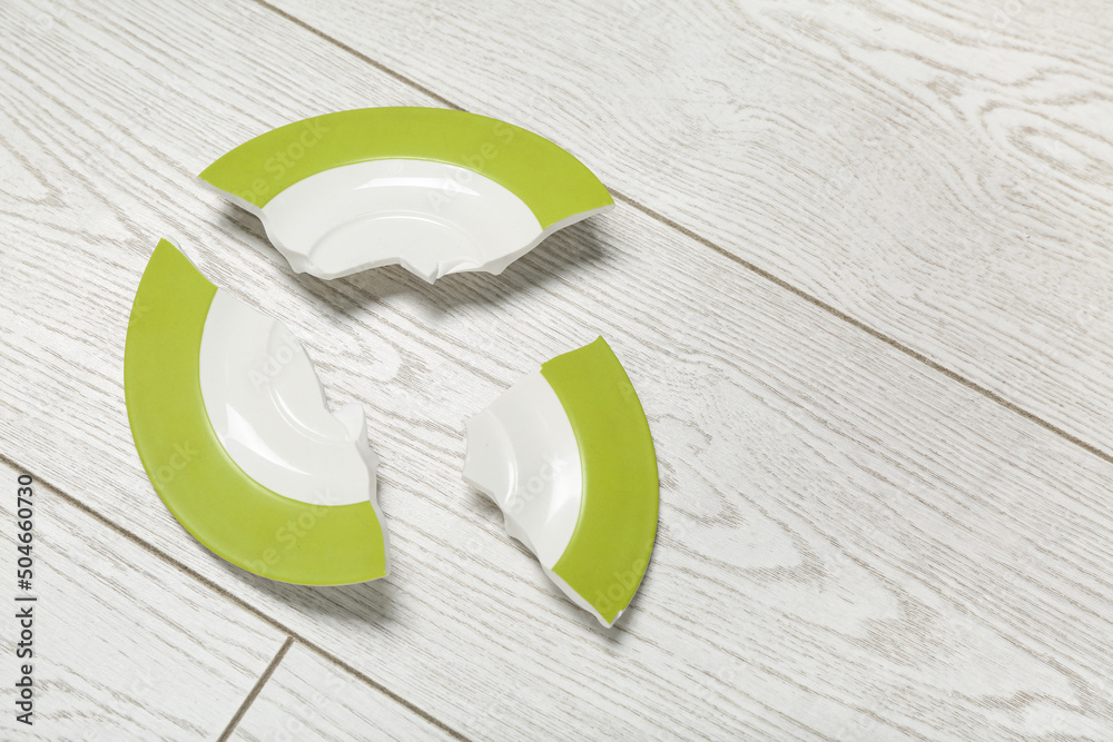 Broken ceramic plate on light wooden background