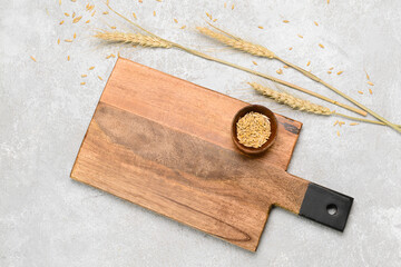 Wooden cutting board and bowl of wheat grains on grey background