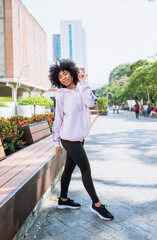 Wall Mural - beauty of afro teenage woman model posing smiling with pink sweatshirt and sportswear in public park