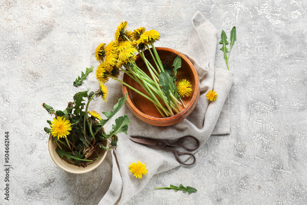 Bowls with yellow dandelions, scissors and napkin on grunge background