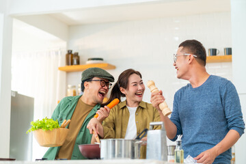 Wall Mural - Asian people friends enjoy cooking pasta in cooking pan with talking together in the kitchen at home. Man and woman having dinner party meeting celebration eating food together on holiday vacation